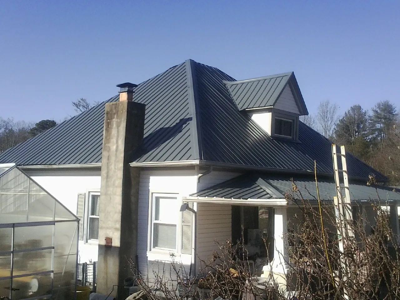 Dark blue standing seam metal roof on a white farmhouse with dormer — Slate & Tile Roof Repair by Roofing Brothers in Montague