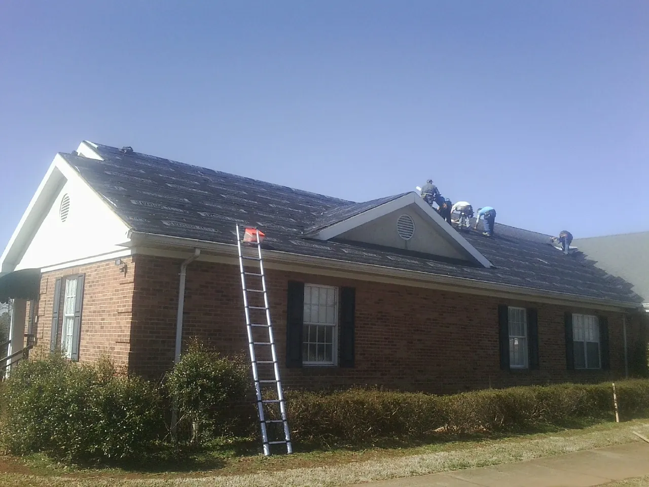 Crew tearing shingles off a brick ranch roof with a ladder set — Metal Roof Repair work by our crew in Montague