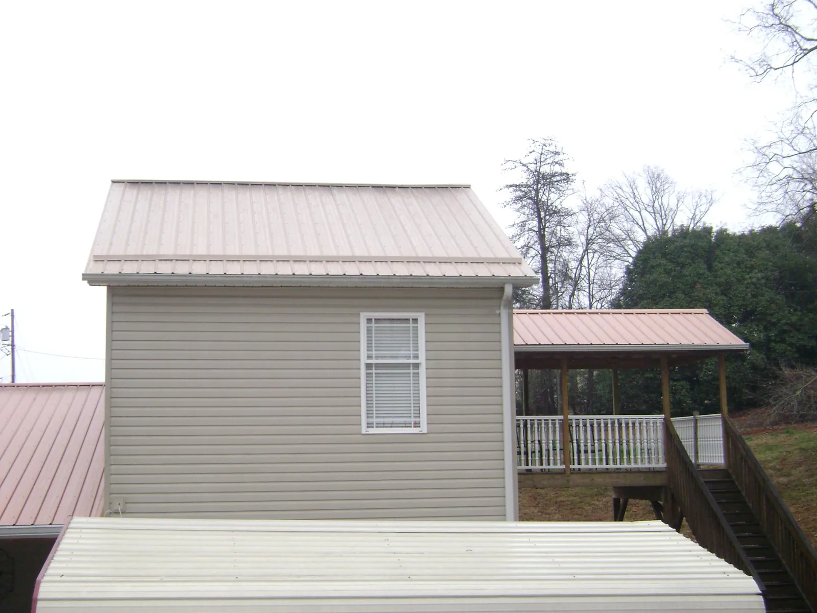 Tan metal roofs on a two story addition and attached porch, from a Roof Replacement job in Montague